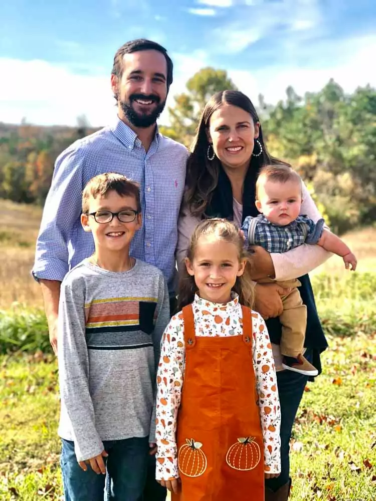 Dr. Jon Byrd of High Point Dental Partners with a family of five standing on grass with trees and a clear sky in the background. The group consists of two adults and three children, dressed in vibrant and diverse outfits that bring life to the scenery. It's a moment filled with warmth and connection amidst a natural and serene setting.