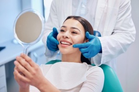 Dental patient examining teeth with mirror during consultation, dentist pointing at smile in modern clinic.