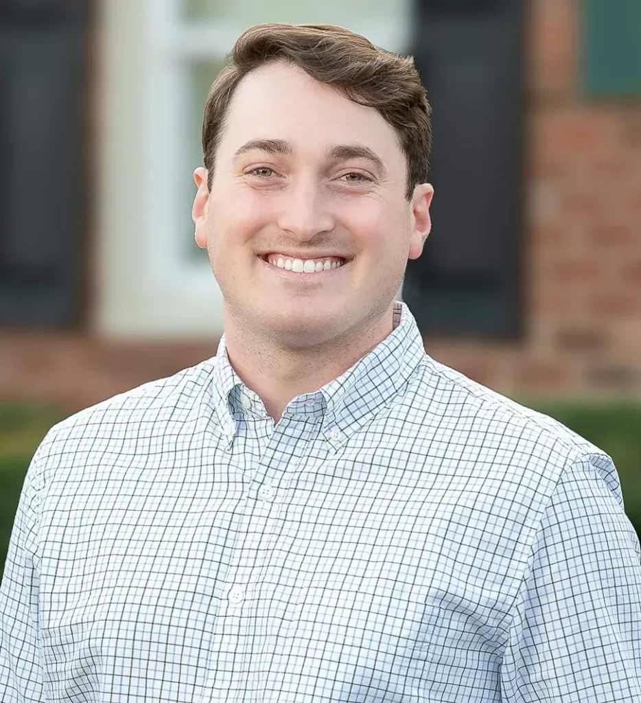 Dr. Jared Floyd smiles in a checkered button-down shirt against an outdoor background, presenting a friendly and professional appearance at High Point Dental Partners.