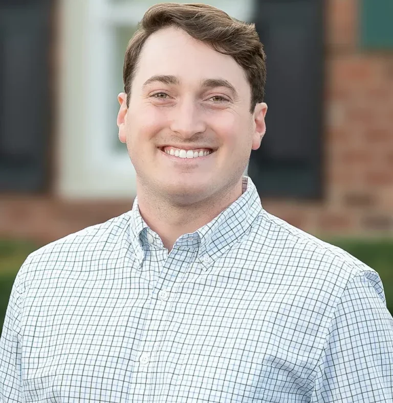 Dr. Jared Floyd smiles in a checkered button-down shirt against an outdoor background, presenting a friendly and professional appearance at High Point Dental Partners.